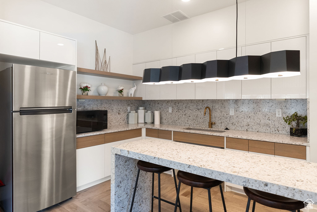 Kitchen with freestanding refrigerator, a sink, white cabinets, modern cabinets, and a breakfast bar area