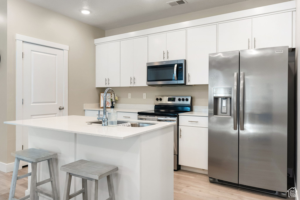 Kitchen featuring white cabinets, stainless steel appliances, light wood-style flooring, a sink, and light countertops