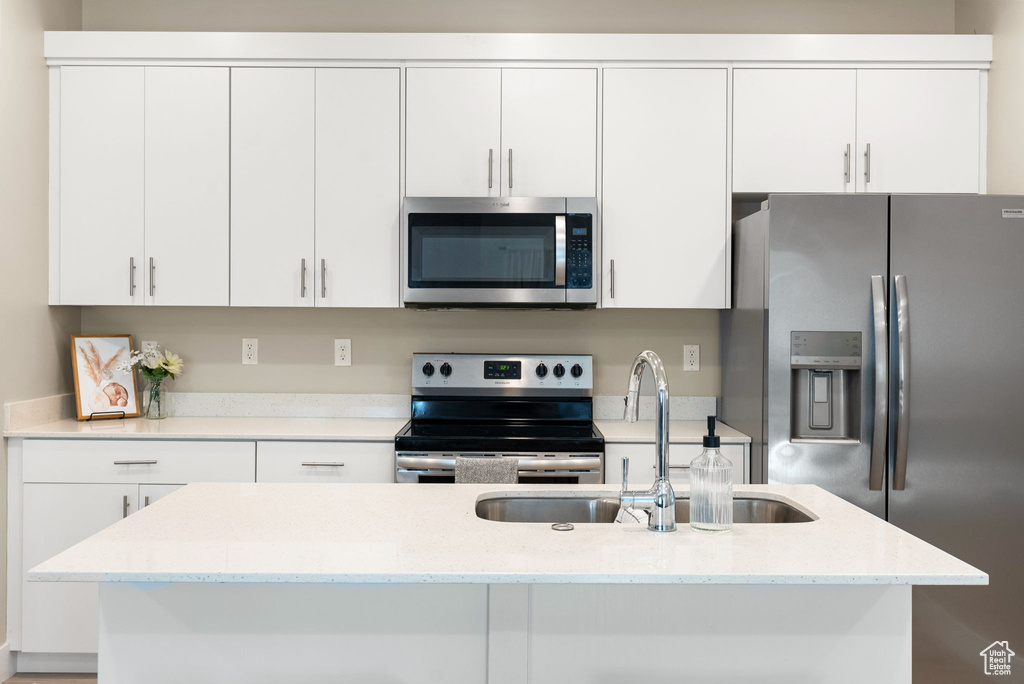 Kitchen with white cabinets, stainless steel appliances, a kitchen island with sink, and a sink