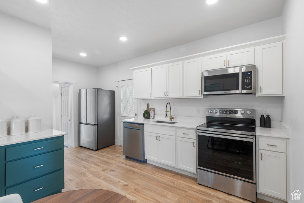 Kitchen with light countertops, white cabinetry, stainless steel appliances, and a sink