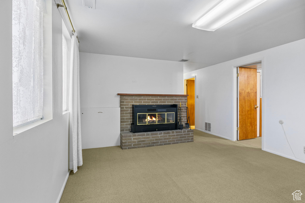 Unfurnished living room featuring a brick fireplace, baseboards, visible vents, and carpet