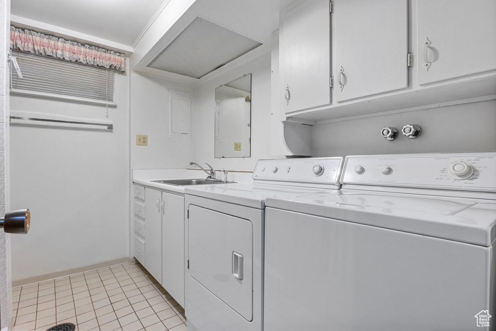 Clothes washing area with washer and dryer, light tile patterned floors, a sink, and cabinet space