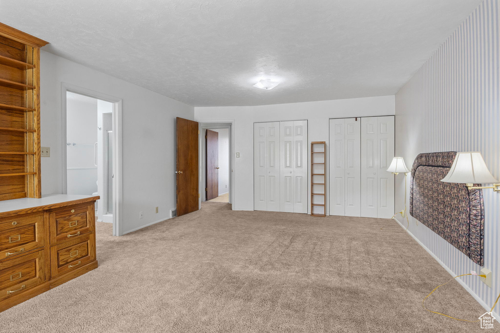 Unfurnished bedroom with connected bathroom, multiple closets, and light carpet