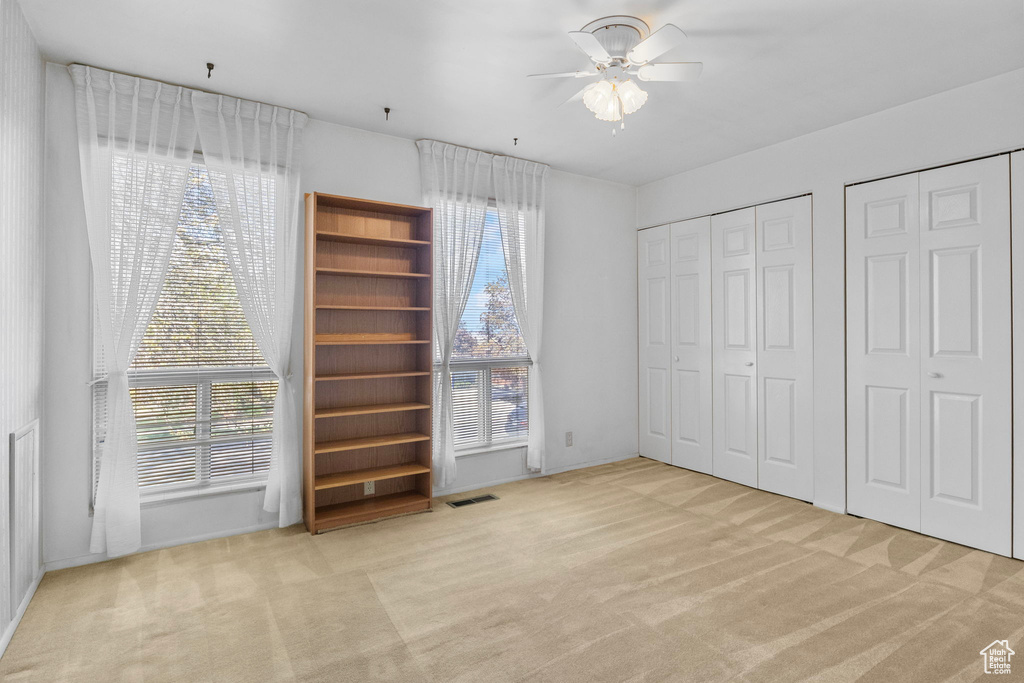 Unfurnished bedroom with carpet floors, ceiling fan, two closets, and visible vents