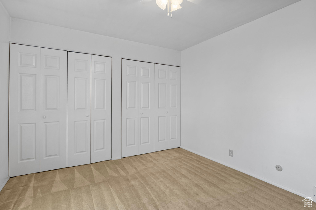 Unfurnished bedroom featuring baseboards, ceiling fan, carpet, and two closets