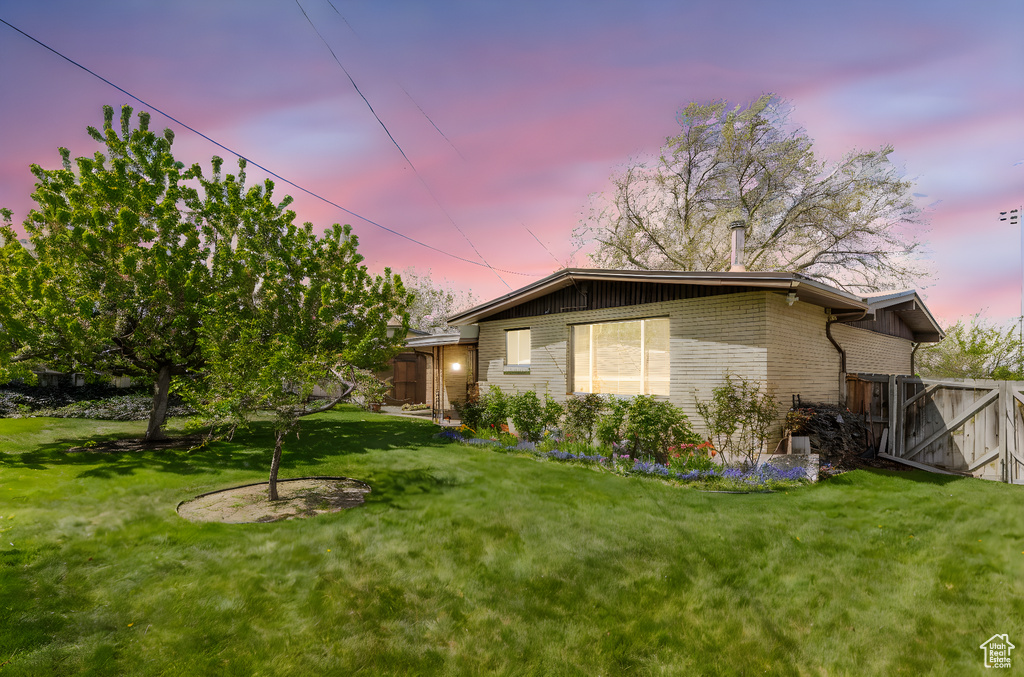 Property exterior at dusk with a yard, brick siding, and fence