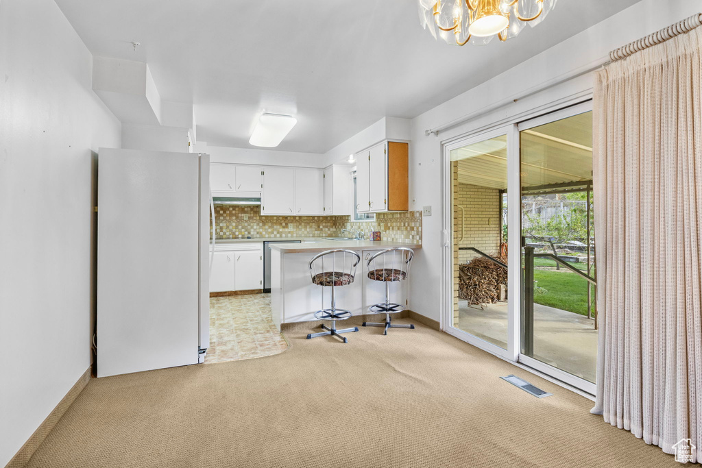 Kitchen featuring light colored carpet, an inviting chandelier, freestanding refrigerator, a peninsula, and visible vents