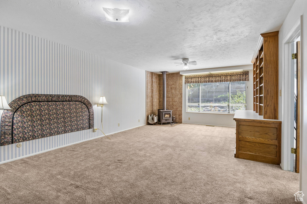 Unfurnished living room with a wood stove, a textured ceiling, ceiling fan, and carpet flooring