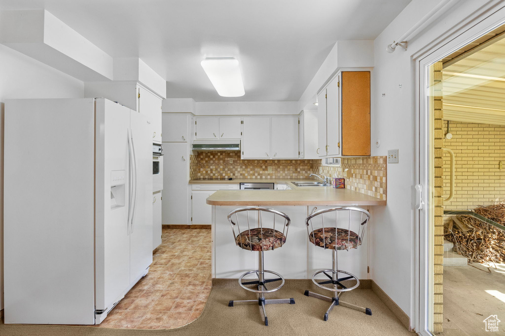 Kitchen with a peninsula, white appliances, under cabinet range hood, a sink, and backsplash