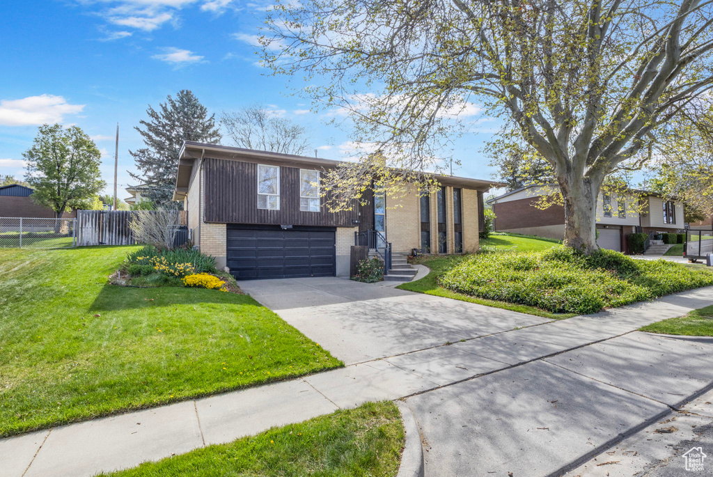 View of front of home with a garage, fence, a front yard, brick siding, and driveway