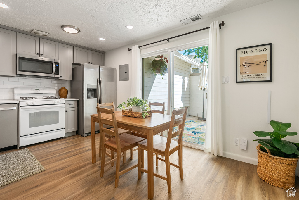Dining space with light wood-type flooring, electric panel, a textured ceiling, baseboards, and recessed lighting