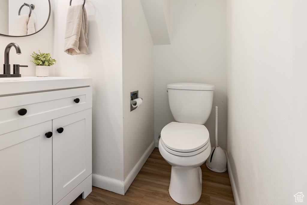 Half bathroom with vanity, toilet, baseboards, and wood finished floors