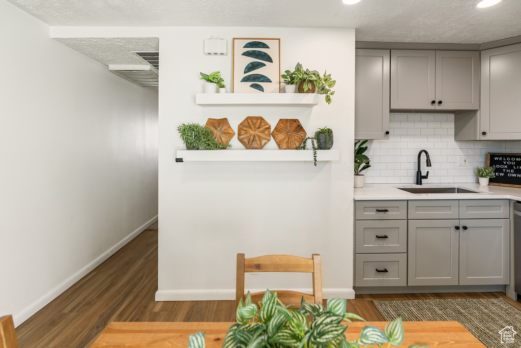 Kitchen featuring gray cabinets, a sink, baseboards, wood finished floors, and a textured ceiling