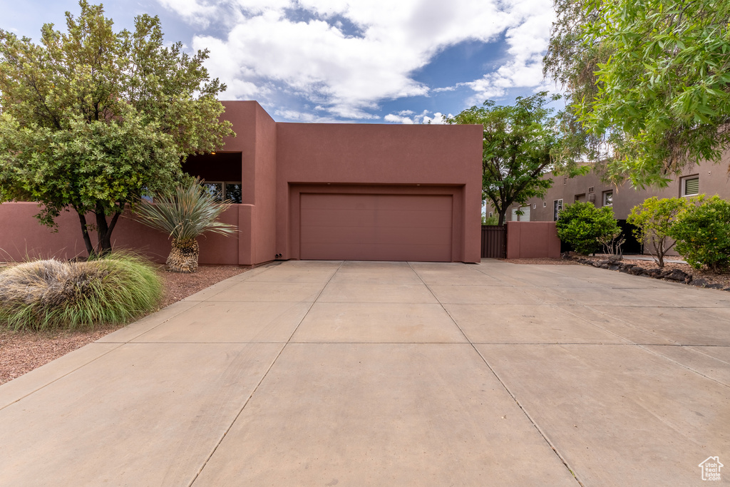 Pueblo revival-style home featuring fence, an attached garage, stucco siding, and concrete driveway