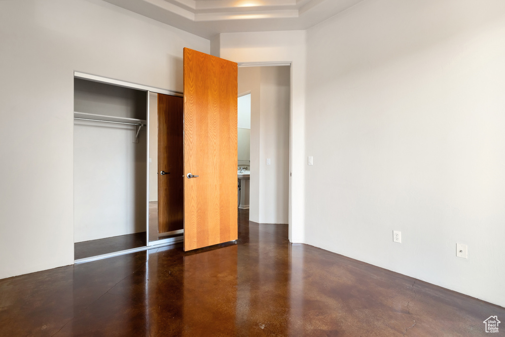 Unfurnished bedroom with finished concrete flooring, a raised ceiling, and a closet