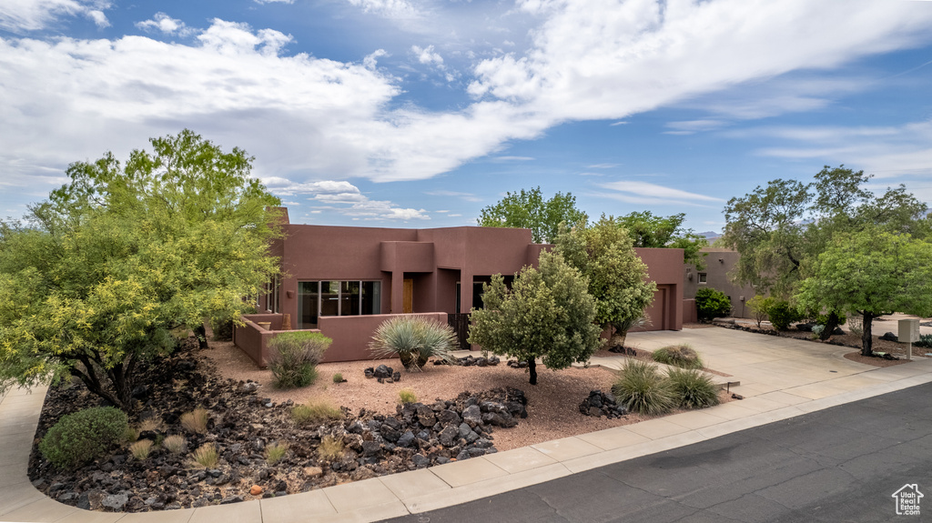 Pueblo revival-style home featuring an attached garage, concrete driveway, fence private yard, and stucco siding