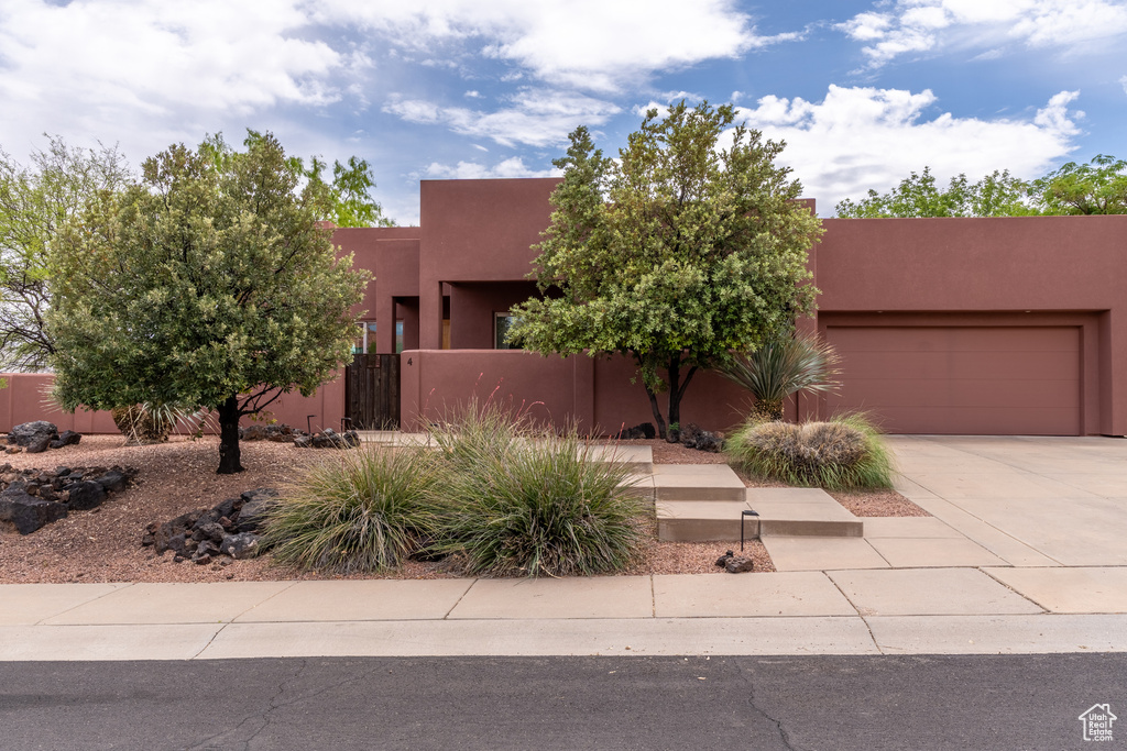 Adobe home featuring an attached garage, stucco siding, driveway, and fence private yard