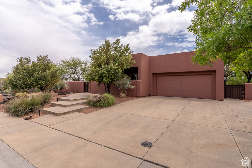 Pueblo-style home featuring an attached garage, stucco siding, and concrete driveway
