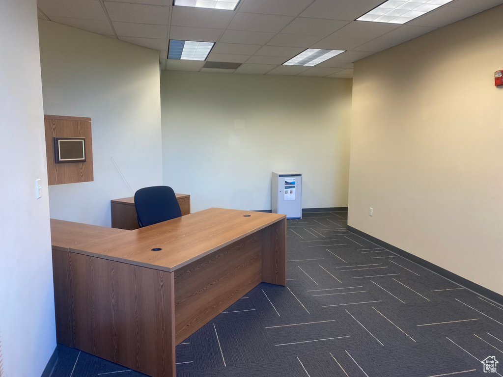 Office area with a drop ceiling, dark colored carpet, and baseboards