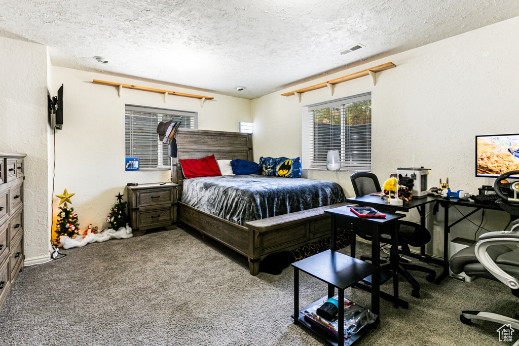 Carpeted bedroom featuring a textured wall, a textured ceiling, and visible vents