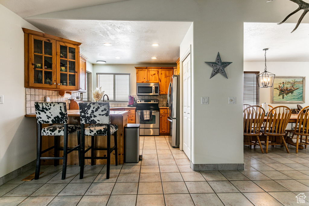Kitchen featuring stainless steel appliances, a peninsula, tasteful backsplash, glass insert cabinets, and a breakfast bar area