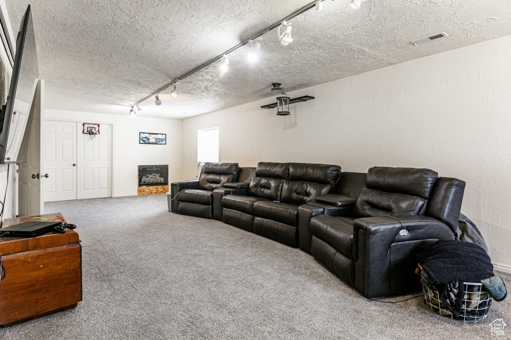 Carpeted home theater with visible vents, a textured ceiling, and rail lighting