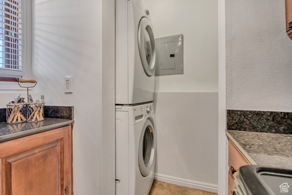 Washroom featuring stacked washing machine and dryer, electric panel, light tile patterned floors, and baseboards
