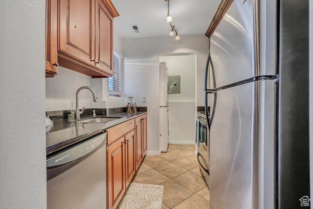 Kitchen featuring appliances with stainless steel finishes, a sink, brown cabinetry, light tile patterned floors, and dark stone countertops