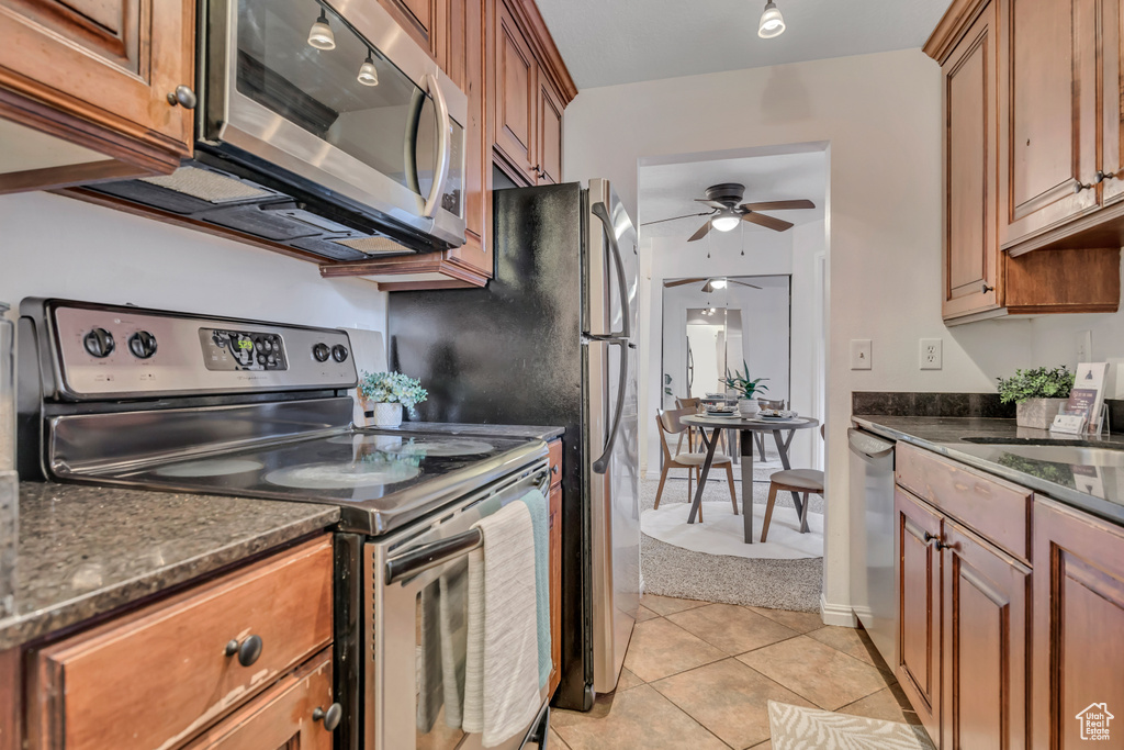 Kitchen with stainless steel appliances, ceiling fan, a sink, light tile patterned floors, and brown cabinetry