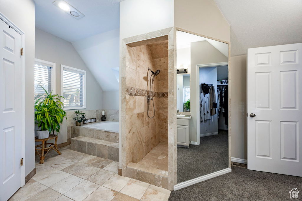 Full bath with a tile shower, a walk in closet, a bath, baseboards, and lofted ceiling