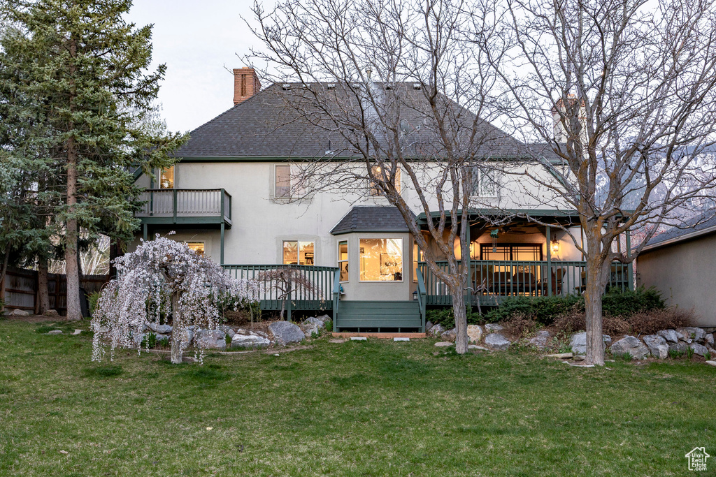 Back of house with roof with shingles, stucco siding, a wooden deck, a chimney, and a lawn