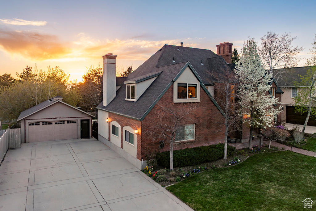 View of front of home with a chimney, a yard, brick siding, an outdoor structure, and a garage