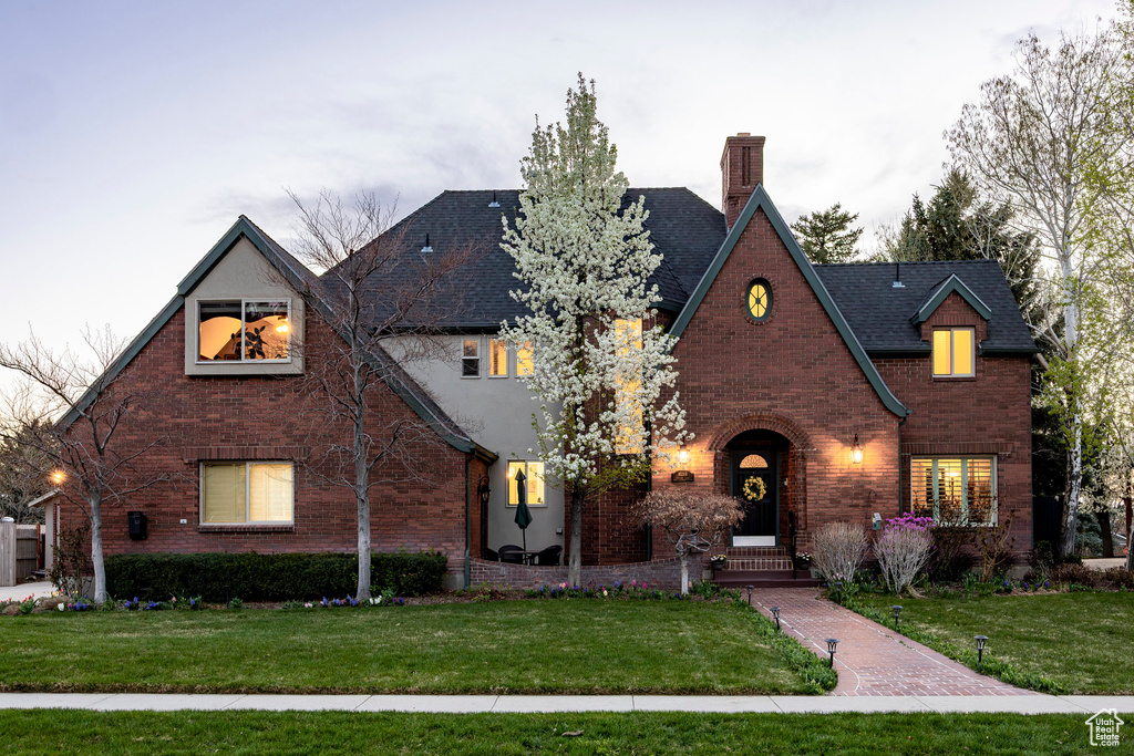 Tudor home featuring roof with shingles, a chimney, brick siding, and a front yard