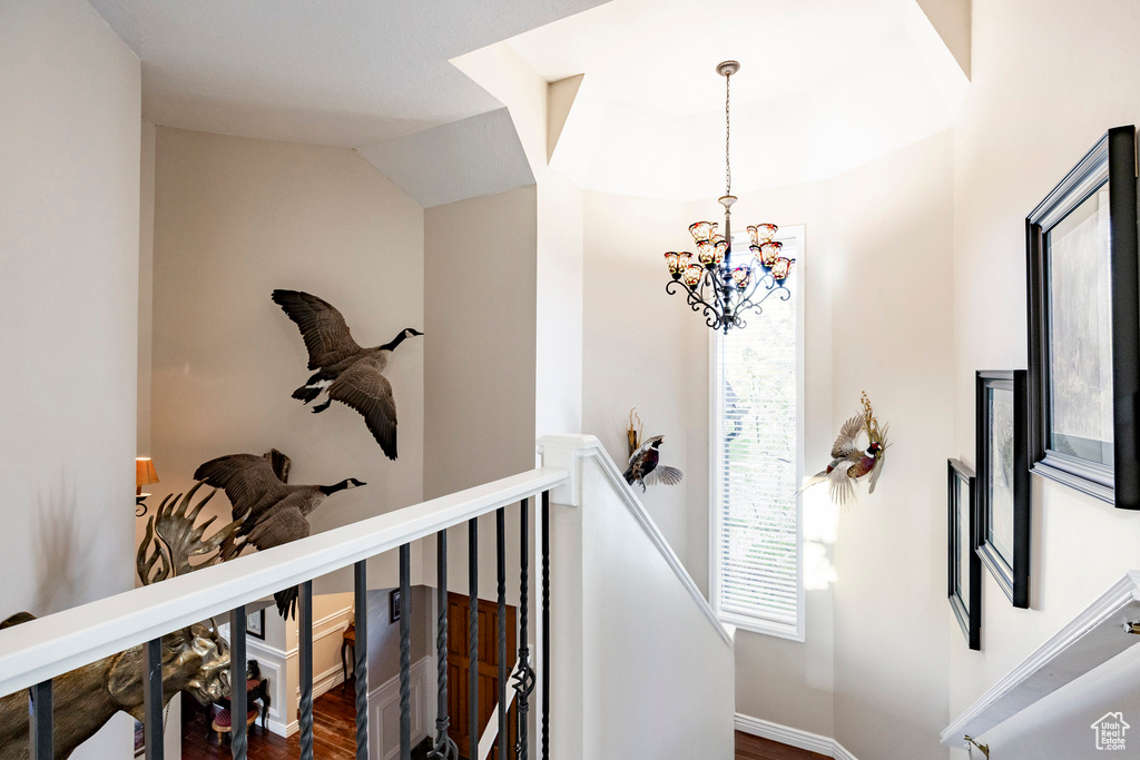 Hallway featuring baseboards, an upstairs landing, a chandelier, and wood finished floors