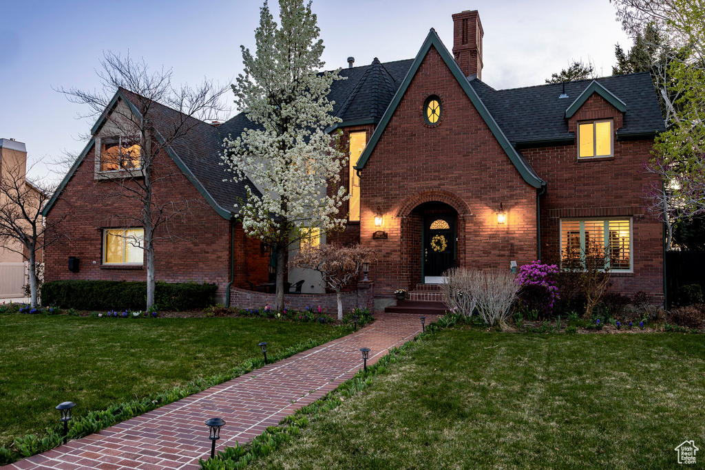 English style home with a front lawn, a shingled roof, brick siding, and a chimney