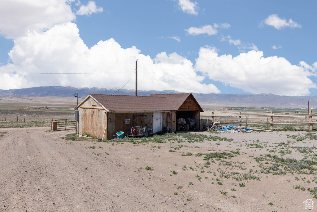 View of outbuilding featuring fence, a rural view, an outdoor structure, and a mountain view