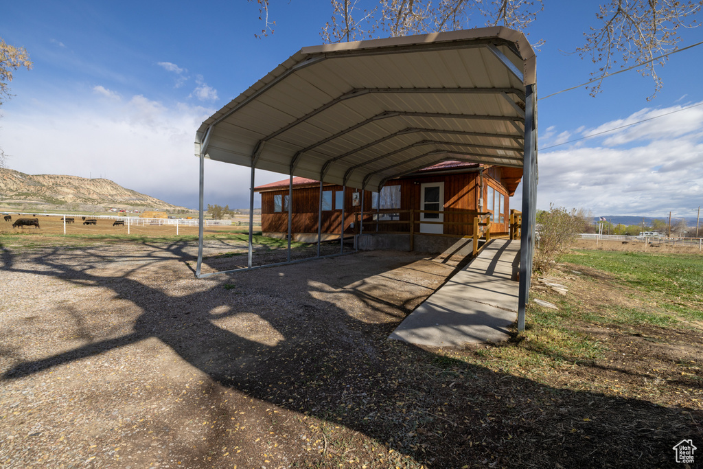 View of parking / parking lot with a detached carport, a rural view, fence, and a mountain view