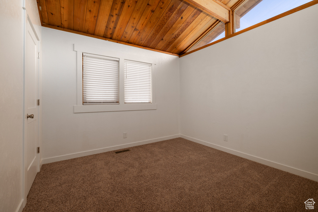 Carpeted spare room with wooden ceiling, baseboards, and lofted ceiling with beams