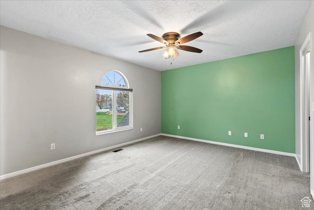 Carpeted empty room featuring baseboards, a ceiling fan, visible vents, and a textured ceiling