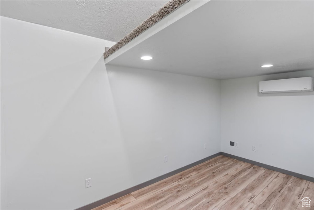 Finished basement featuring recessed lighting, light wood-type flooring, an AC wall unit, and baseboards