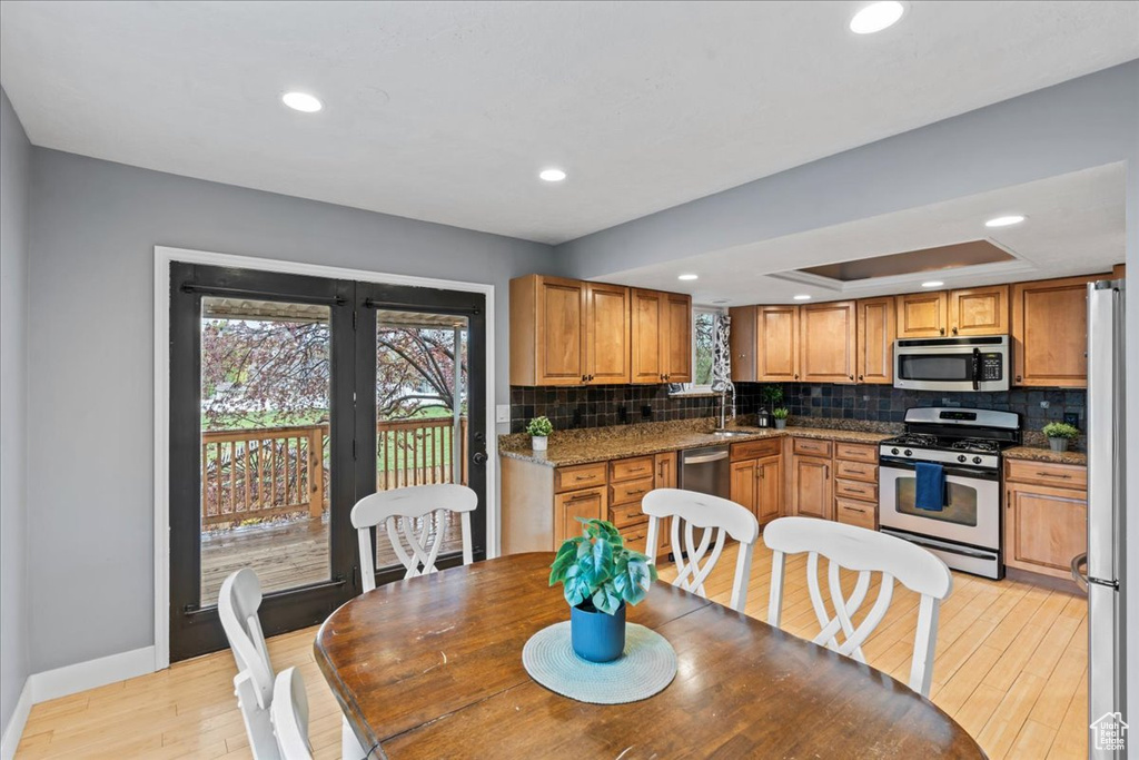 Kitchen with tasteful backsplash, a sink, light wood-style floors, baseboards, and appliances with stainless steel finishes