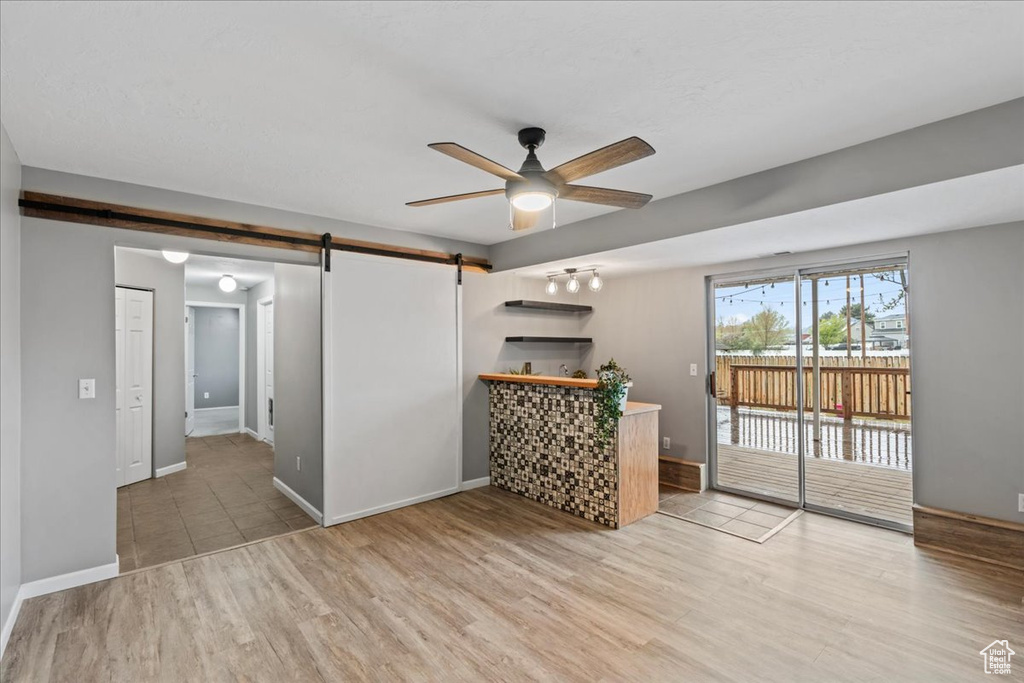 Unfurnished living room featuring light wood-type flooring, baseboards, ceiling fan, and a barn door