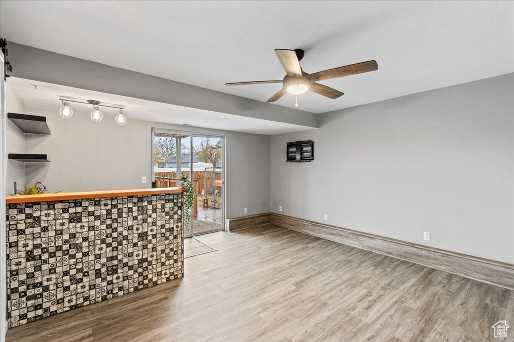 Interior space featuring a ceiling fan, baseboards, bar, and light wood-style flooring