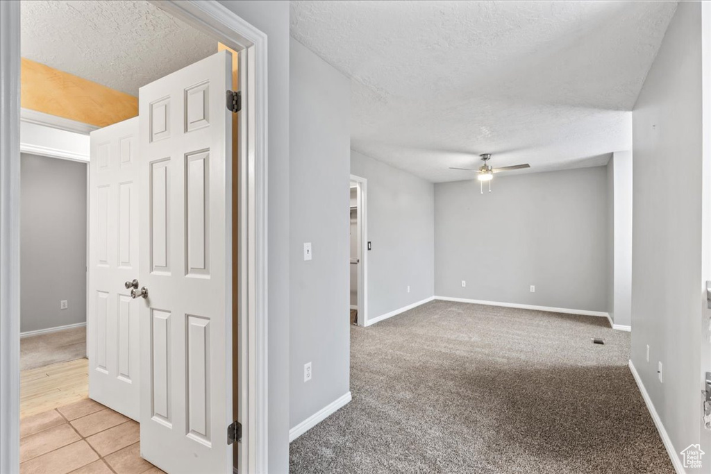 Carpeted spare room featuring a textured ceiling, a ceiling fan, and baseboards