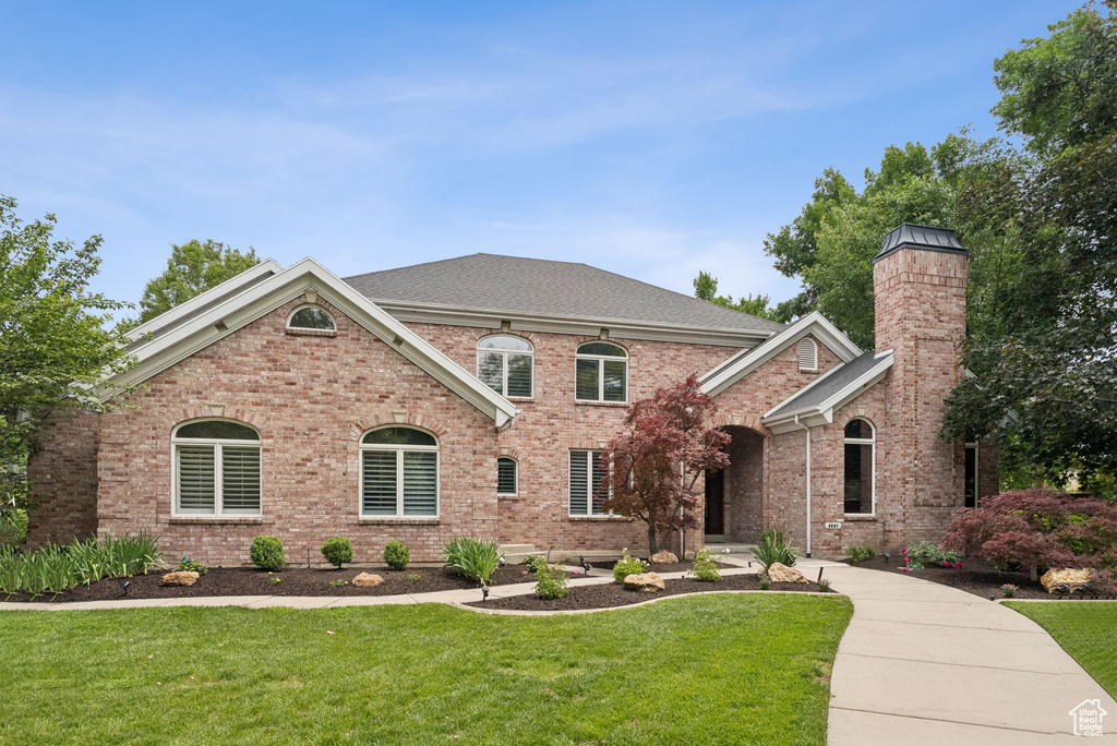 View of front of property with a front lawn, brick siding, and a chimney