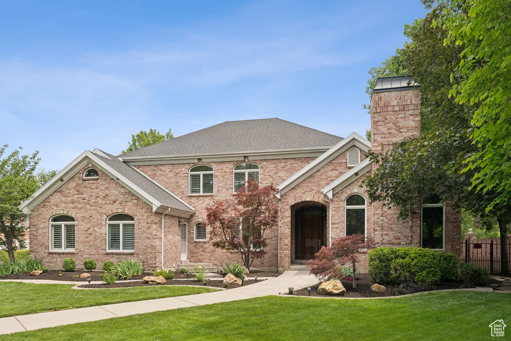 View of front facade featuring brick siding, a shingled roof, and a chimney