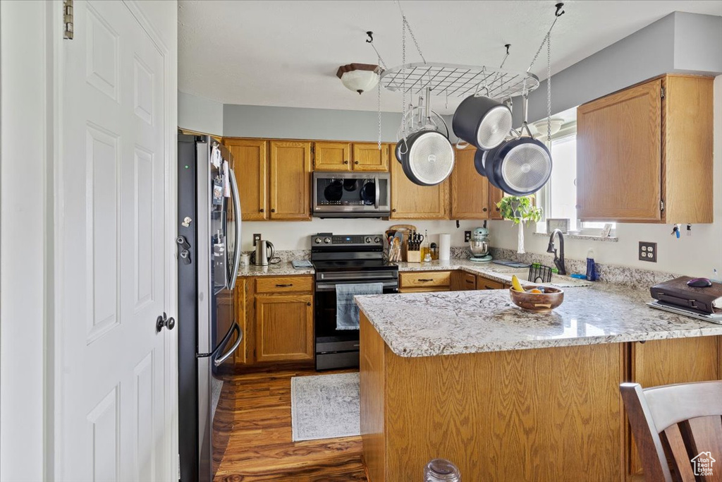 Kitchen with dark wood finished floors, a sink, light stone countertops, a peninsula, and appliances with stainless steel finishes
