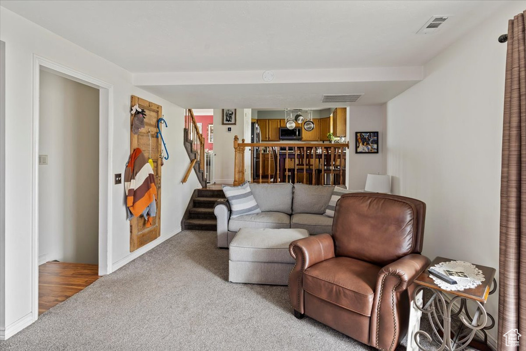 Carpeted living room featuring baseboards, visible vents, and stairs