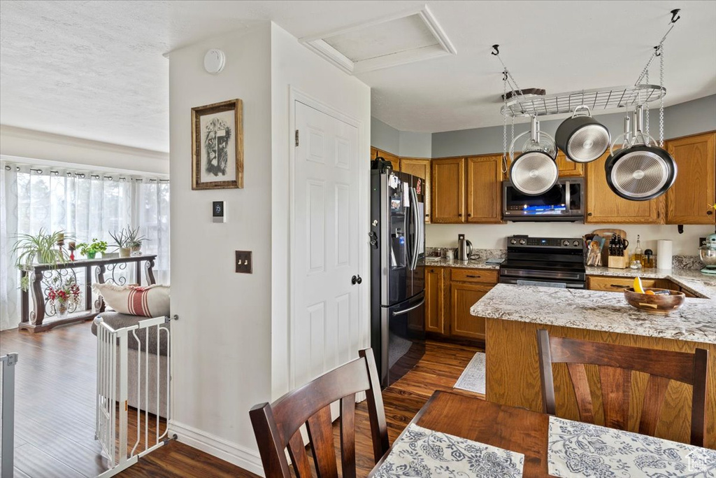 Kitchen with brown cabinets, stainless steel appliances, dark wood finished floors, baseboards, and light stone countertops