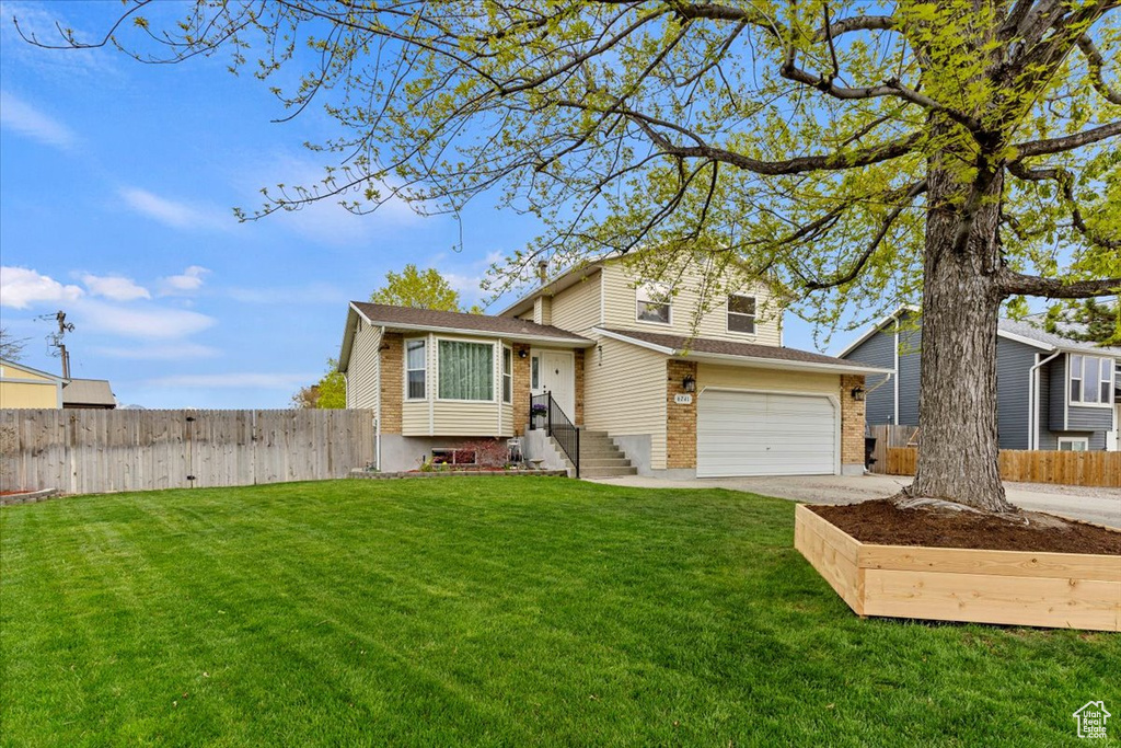 Tri-level home with a front yard, an attached garage, concrete driveway, and fence